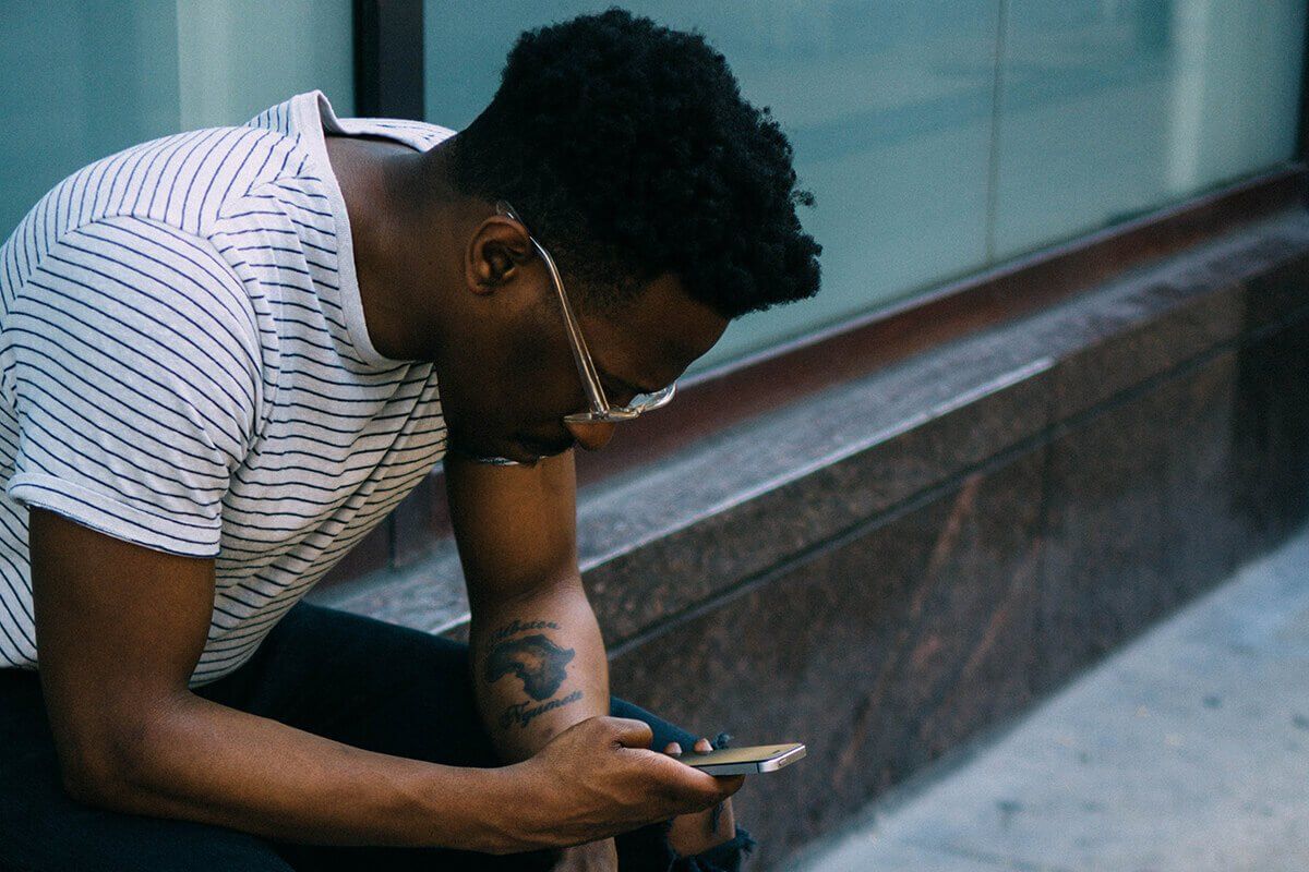 A man is sitting down and looking down at a mobile phone in his hand.