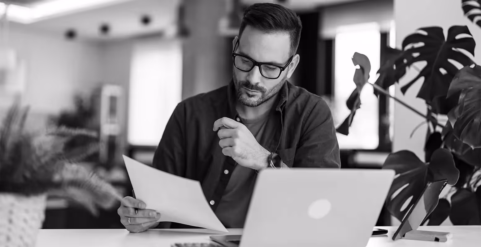 Man sitting at a desk in front of laptop looking at a sheet of paper