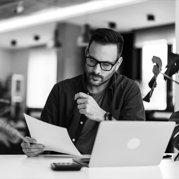 Man sitting at a desk in front of laptop looking at a sheet of paper