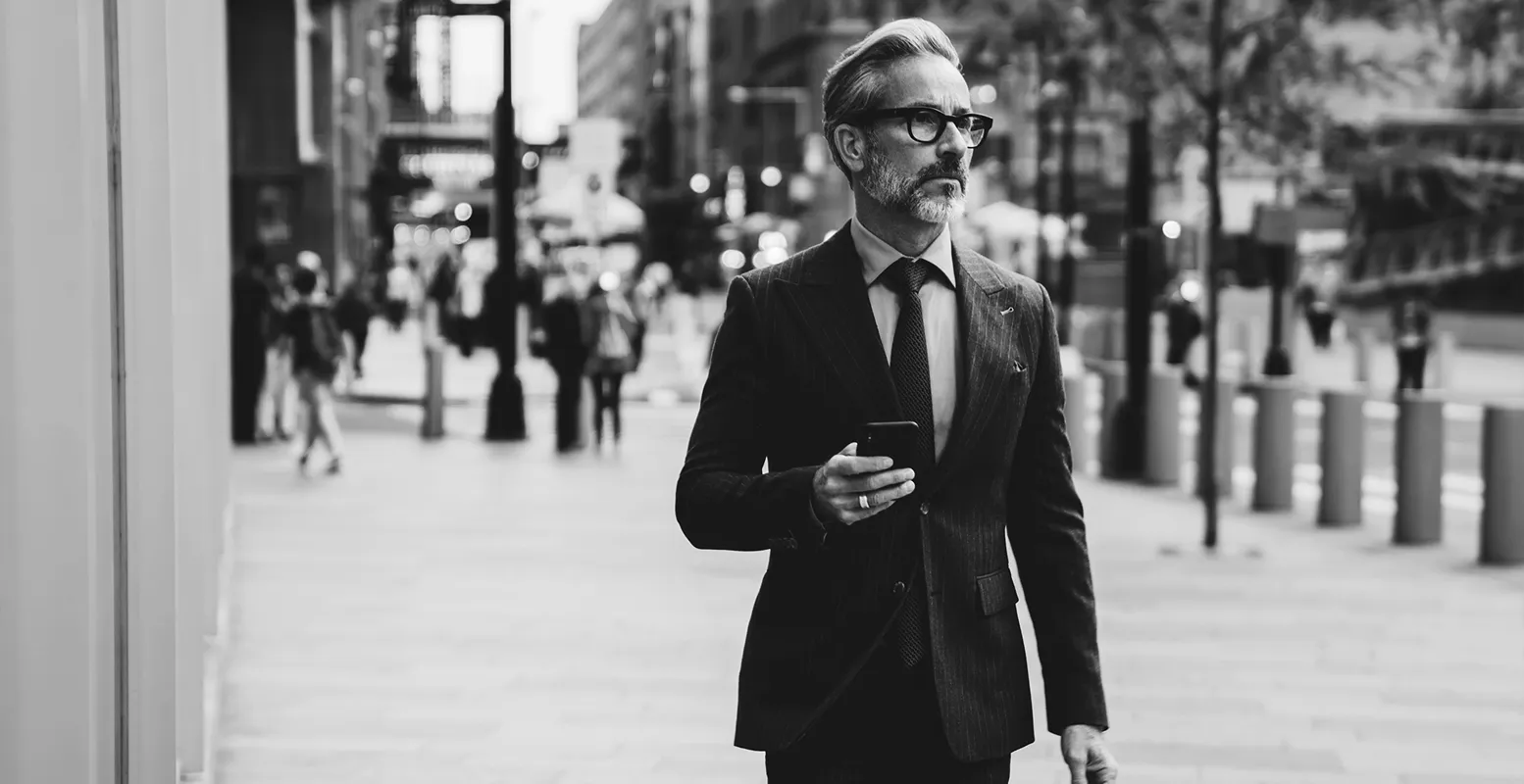 Older business man walking through the city holding a cellphone