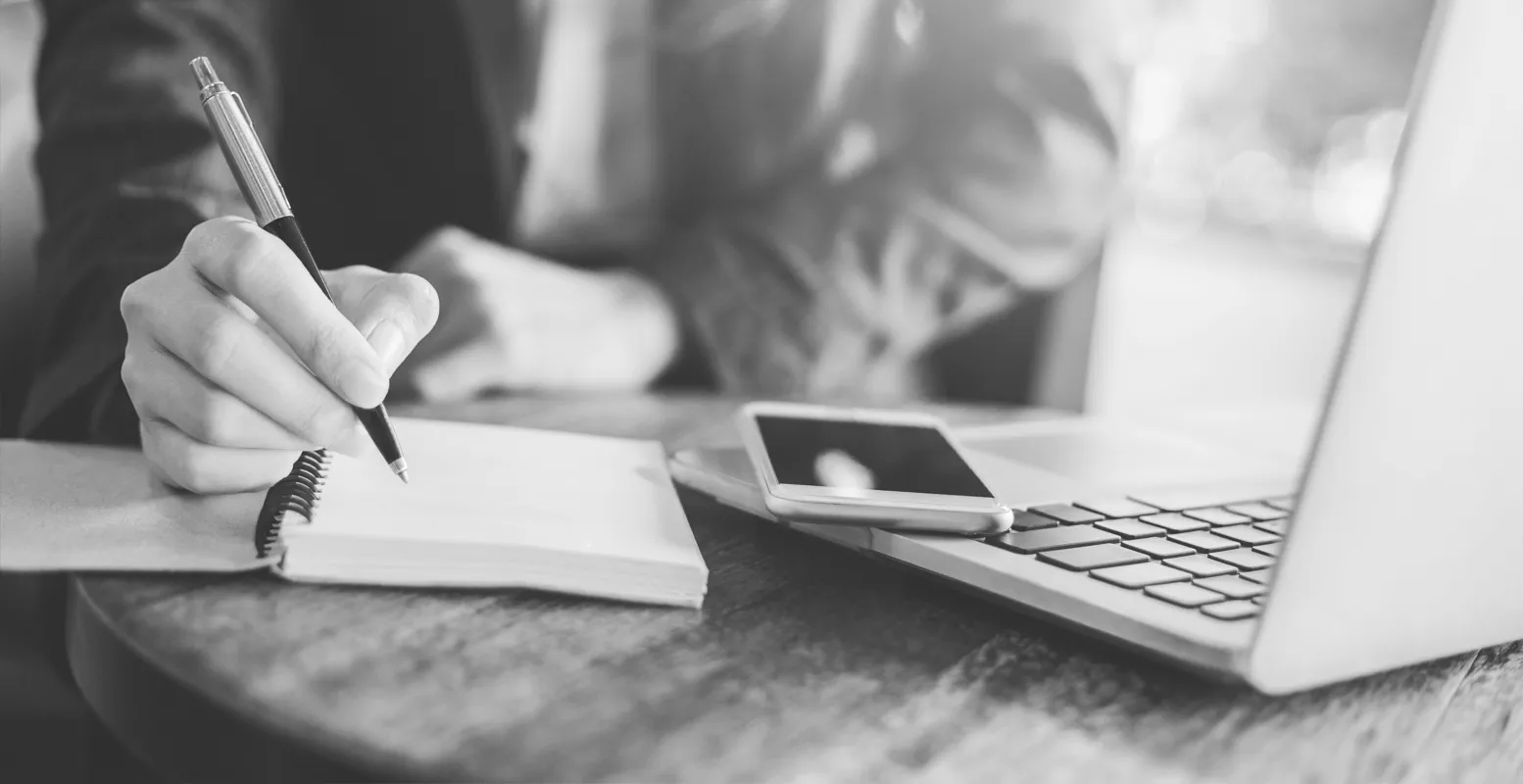 Business man sitting in front of a laptop writing in a notebook