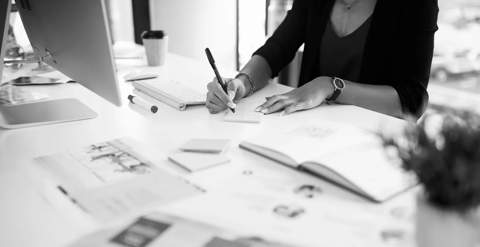 Business woman sitting at a computer desk writing in a notebook