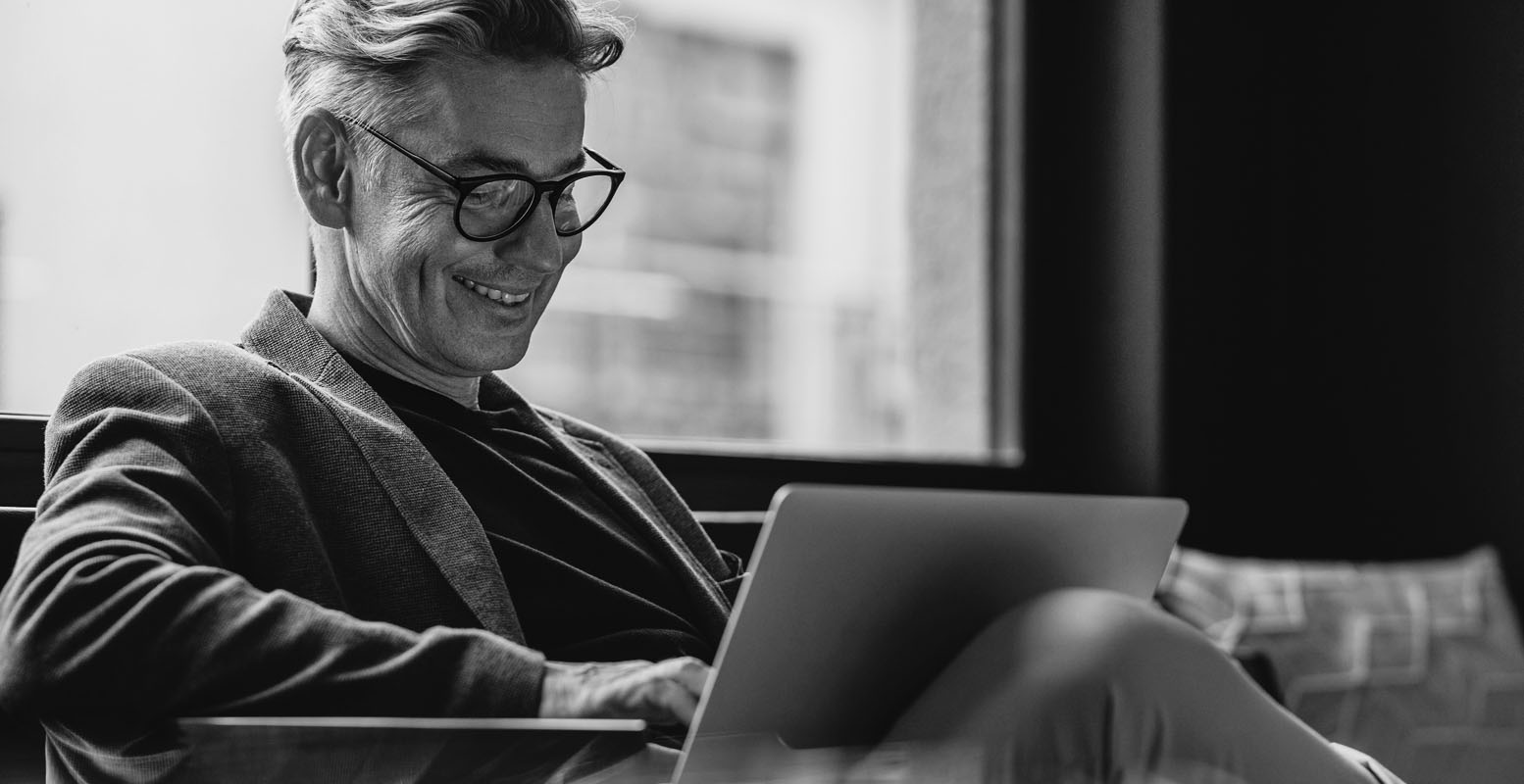 Man sitting on a couch smiling working on a laptop