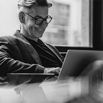 Man sitting on a couch smiling working on a laptop
