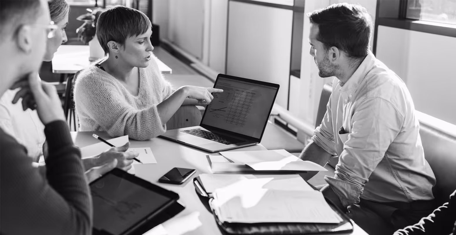 Professionals sitting around table with papers looking at computer screen