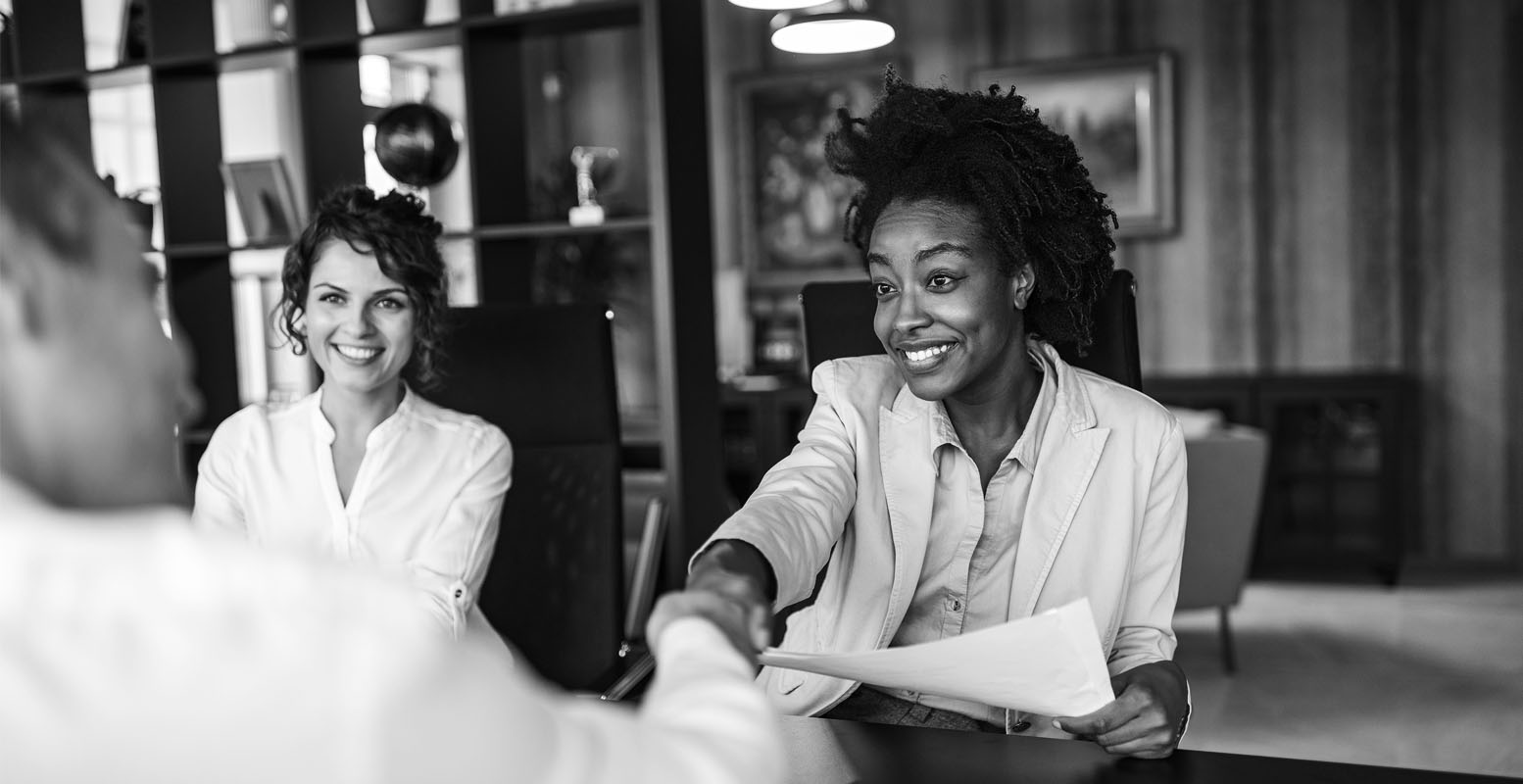 Three professionals sitting across from each other and two of them shaking hands
