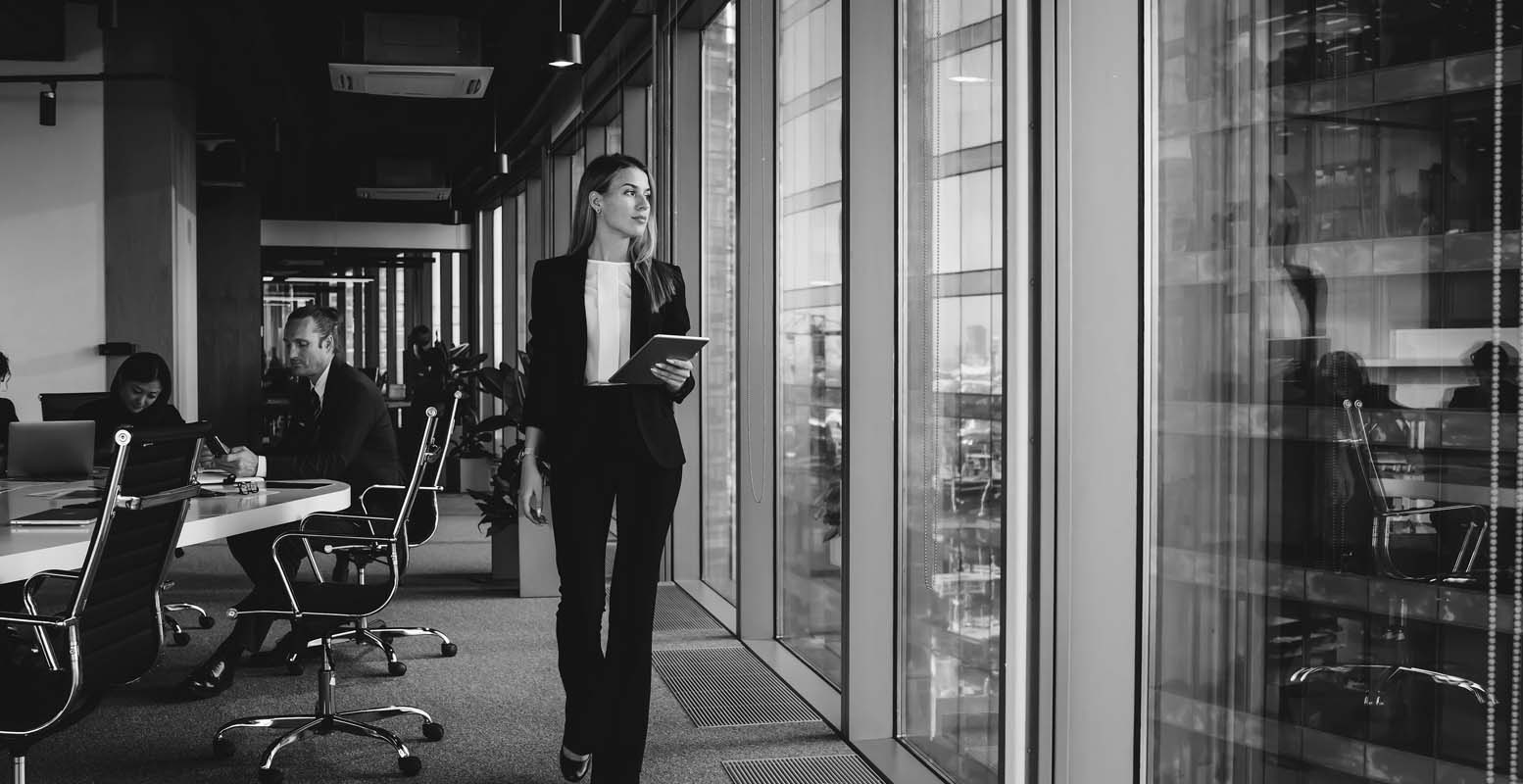 Business woman looking out an office window holding an Ipad