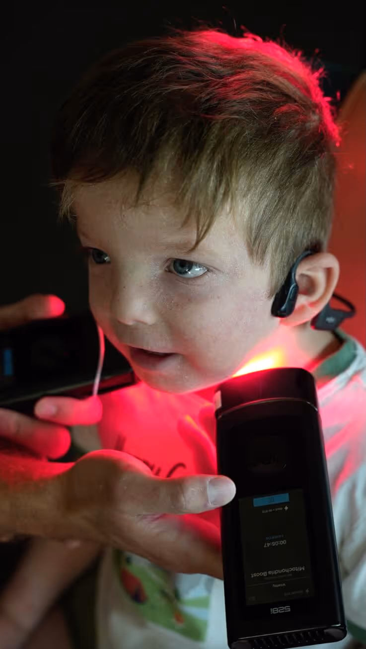 Child with a hearing aid receiving red light laser therapy on the neck.