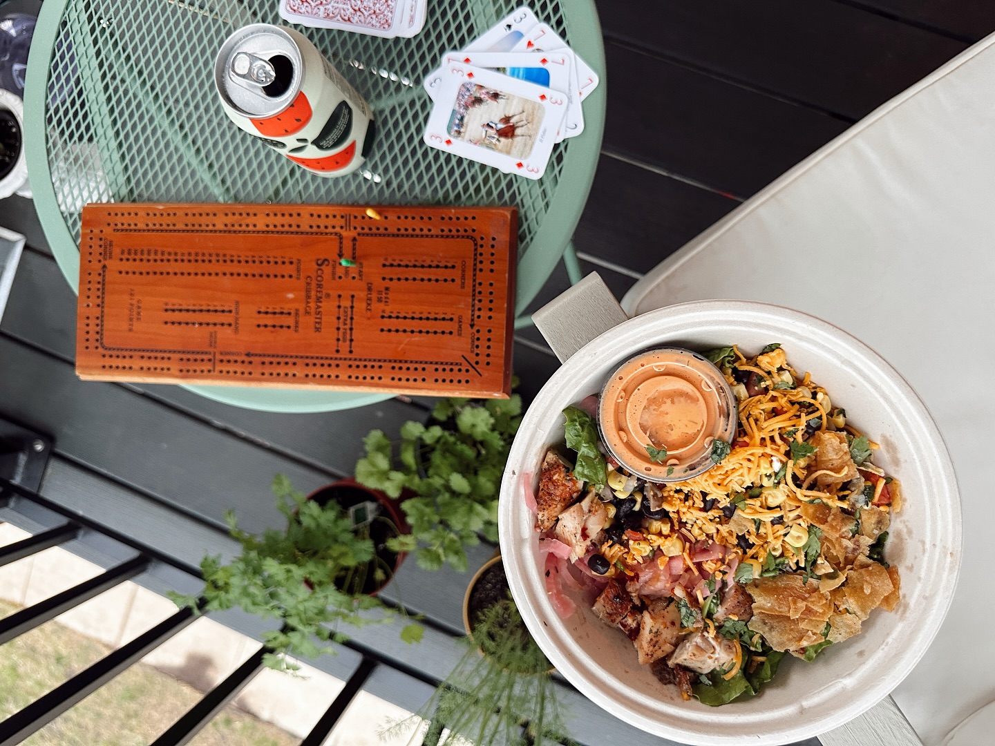 A Forage Kitchen bowl, tepache can, cribbage board, and playing cards on an outdoor table.