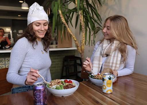 Two women, one in a white beanie and the other in a plaid scarf, happily eat Cobb salads in Forage Kitchen.