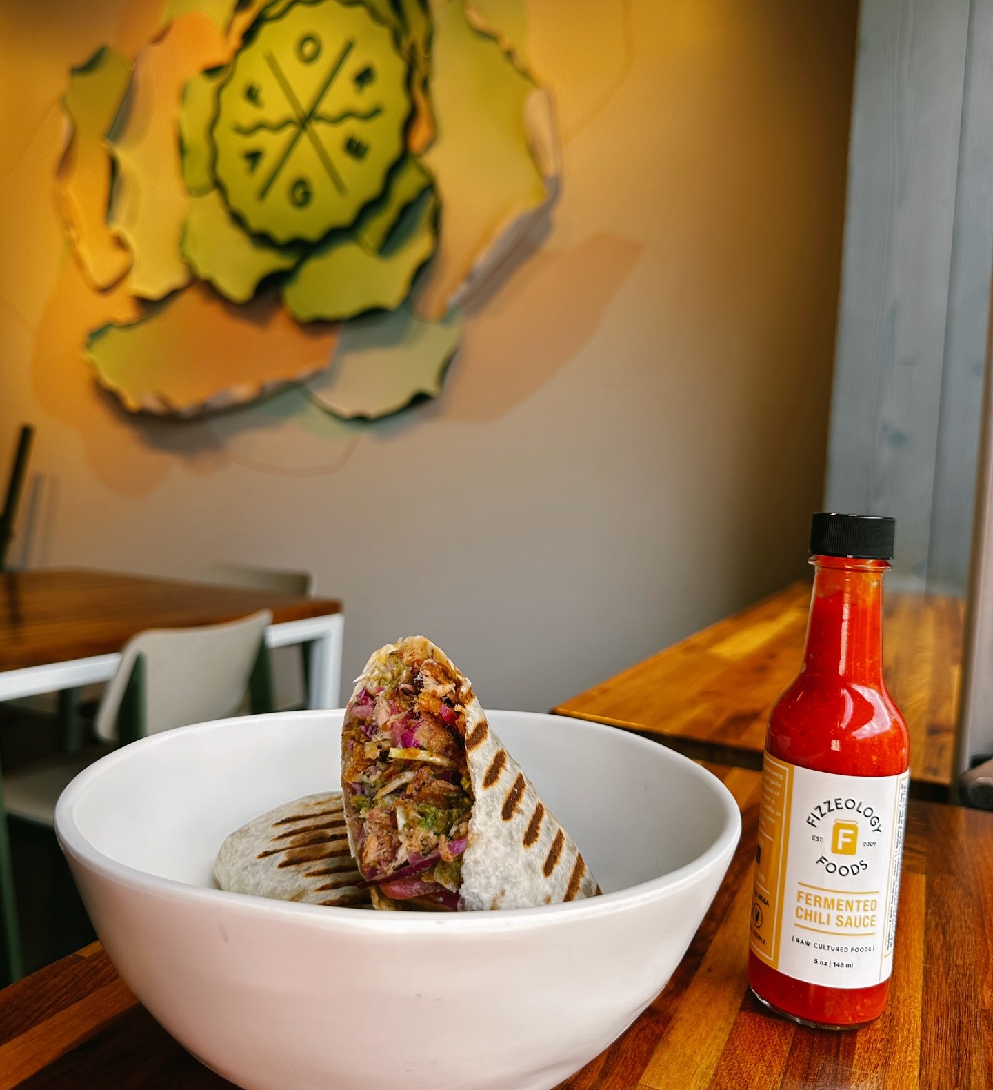 Two Forage Kitchen wraps in a white bowl on a table, accompanied by fermented hot sauce.