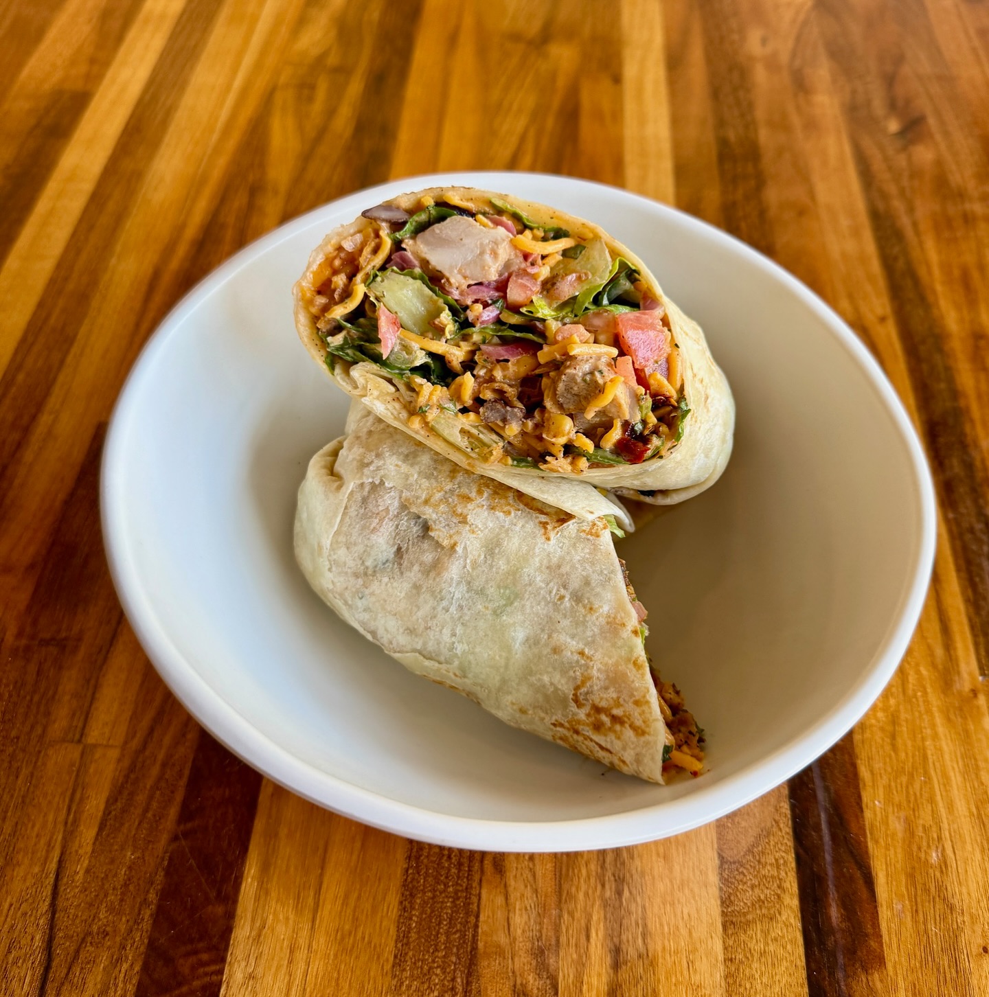 Chicken wrap cut in half, filled with veggies and cheese, served in a white bowl.
