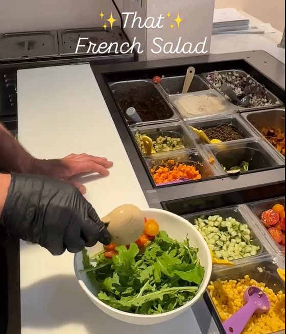 A Forage Kitchen team member builds “That French Salad” with fresh greens and colorful toppings at the salad bar.