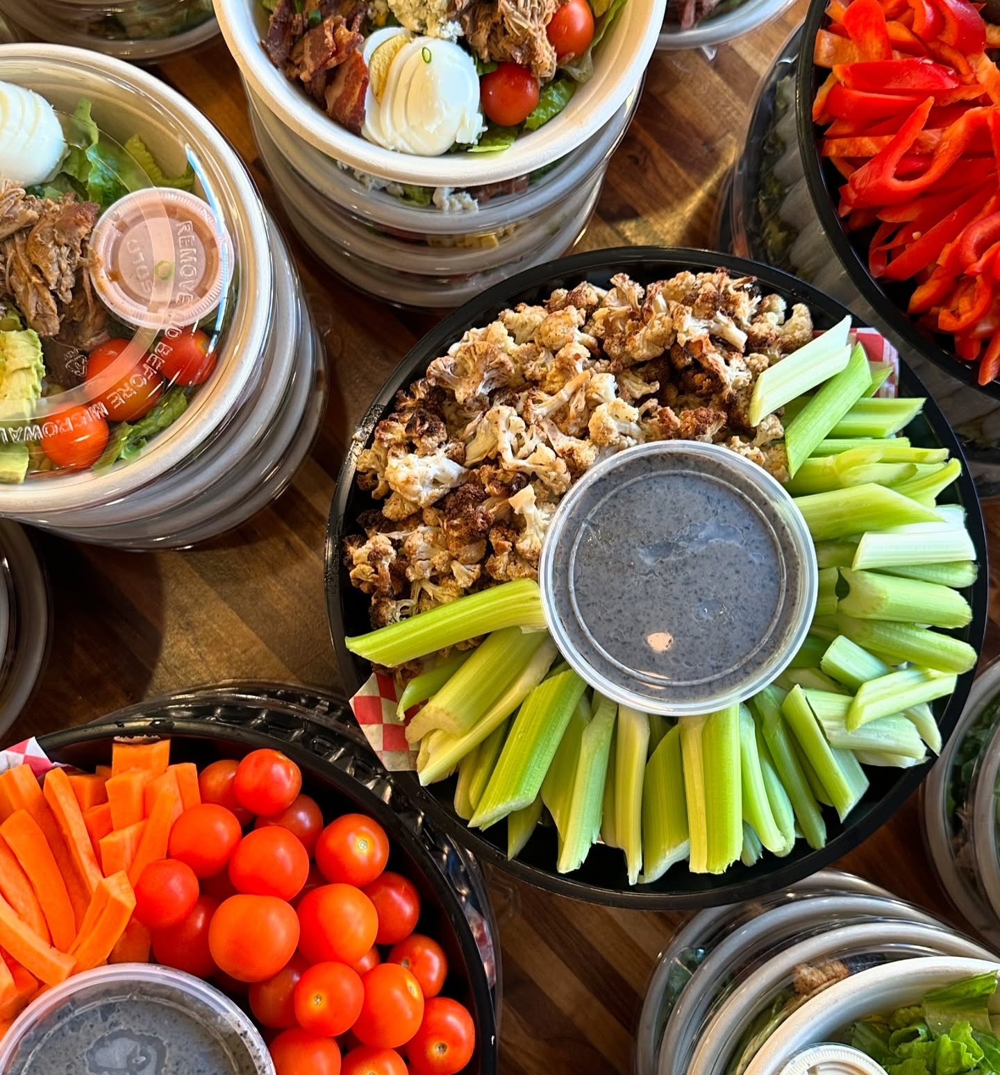 Forage Kitchen catering spread with individual salads and appetizer platters of fresh celery, carrots, and cherry tomatoes.