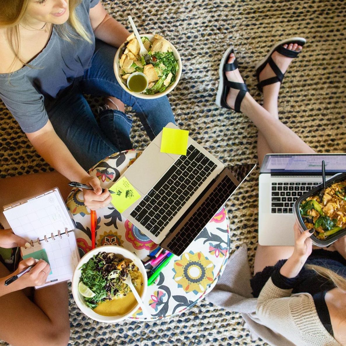 Three female colleagues brainstorming with laptops, sticky notes, and notebooks while enjoying Forage Kitchen bowls.