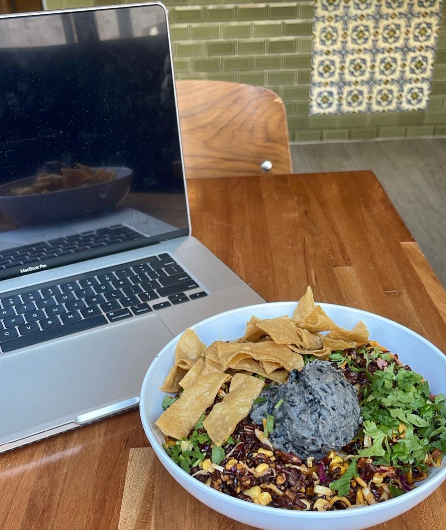  Forage Kitchen grain bowl with tortilla chips beside a laptop on a wooden desk. 