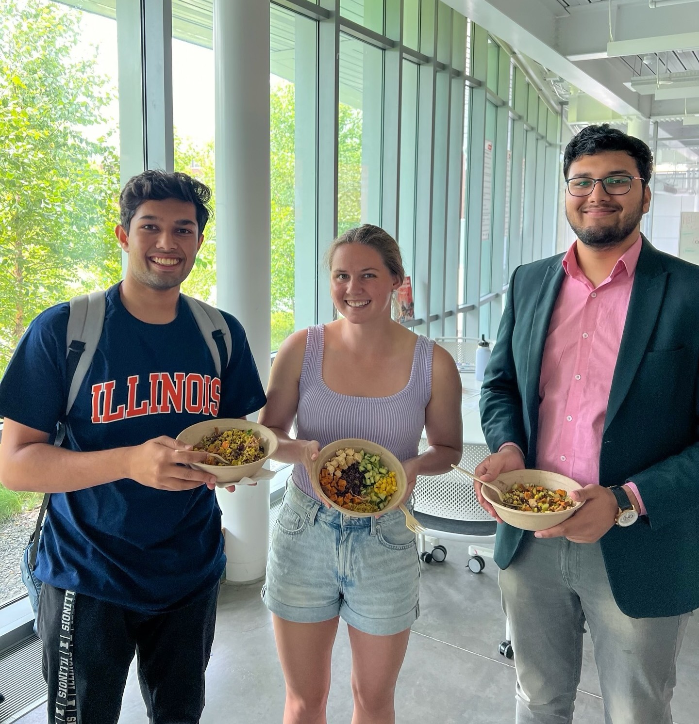 Three smiling colleagues hold grain bowls from Forage Kitchen at a university  event.