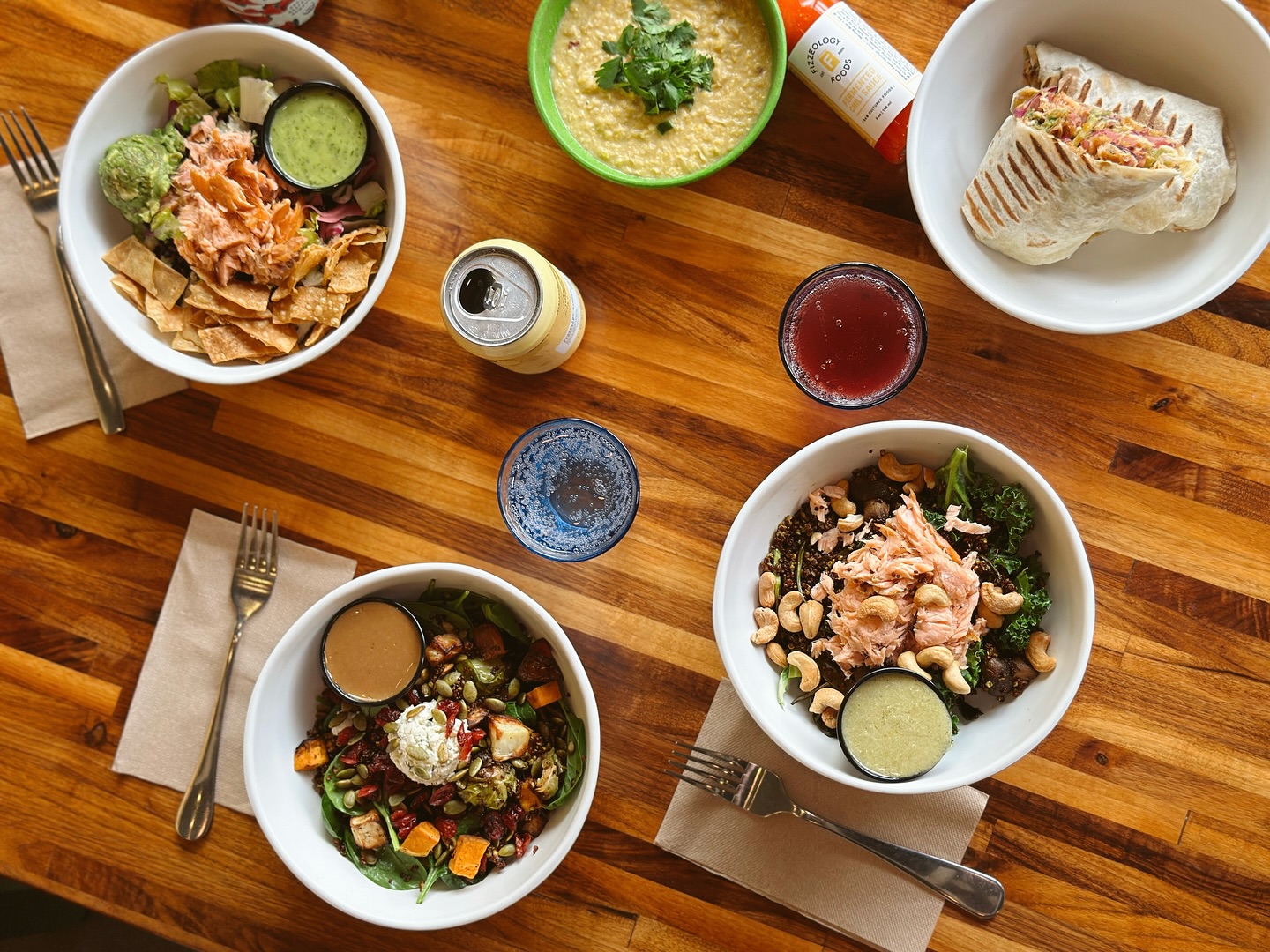 Bowls of food, featuring quinoa, salmon, and vegetables, plus a wrap on a table at Forage Kitchen.