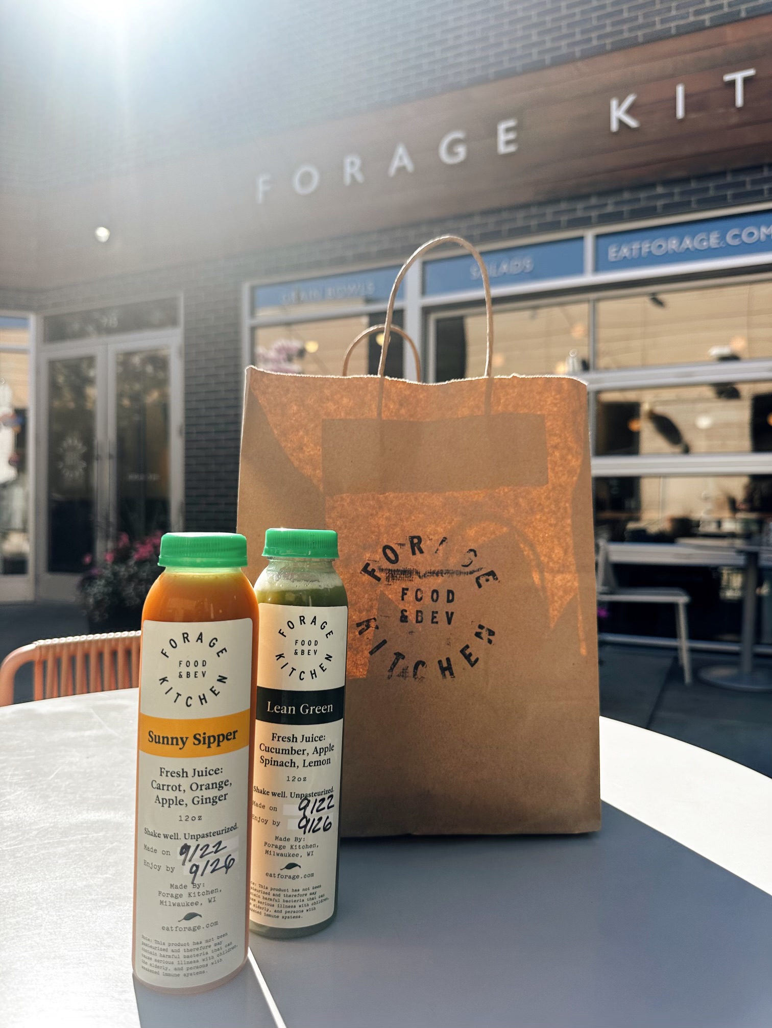 A Forage Kitchen takeout bag with fresh juice bottles, showcasing eco-conscious, compostable packaging.