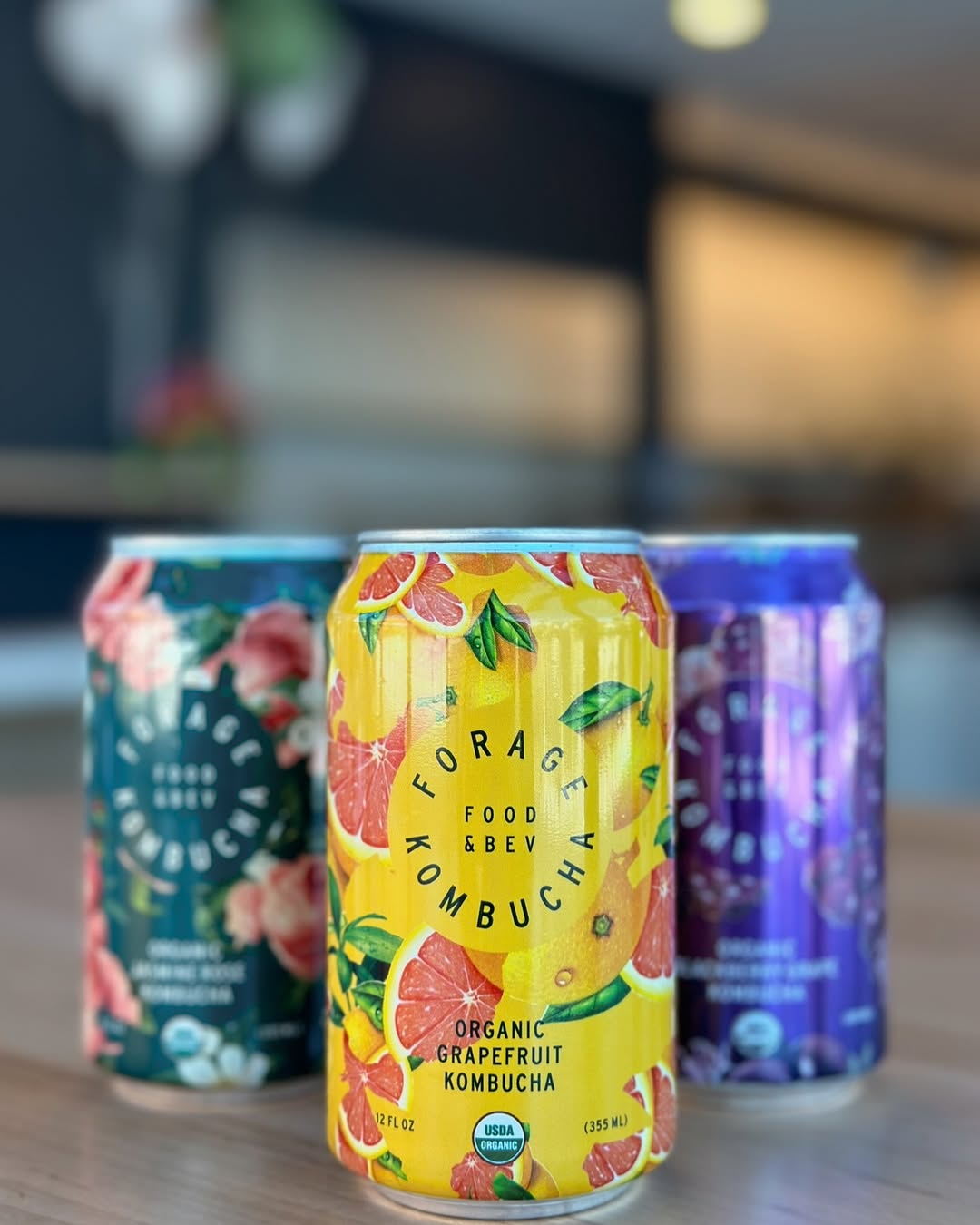 Close-up of three Forage Kombucha cans—Grapefruit, Blackberry, and Jasmine Rose—displayed on a table.