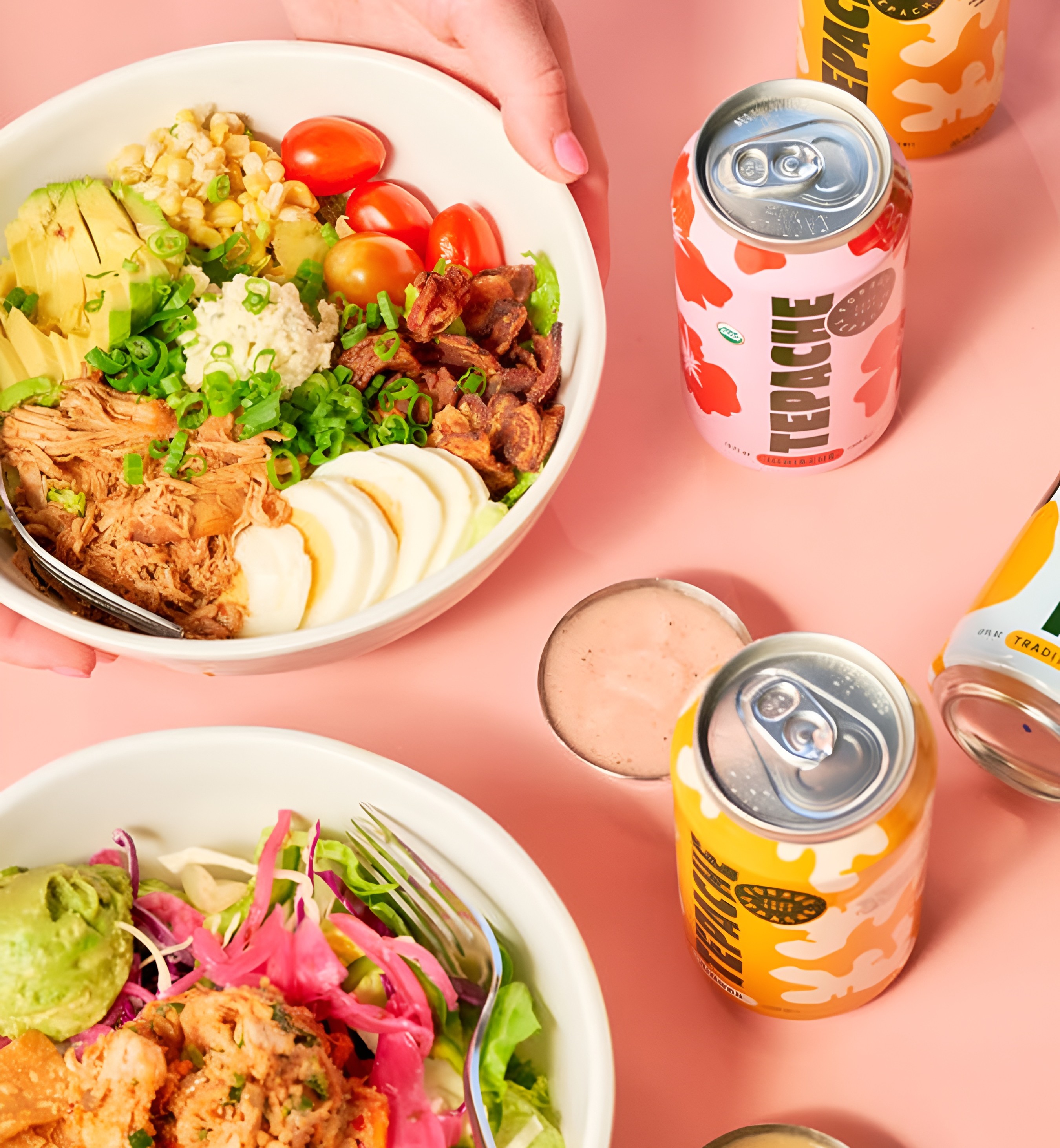 Forage Kitchen catering featuring two salad bowls and several cans of Tepache on a pink background.