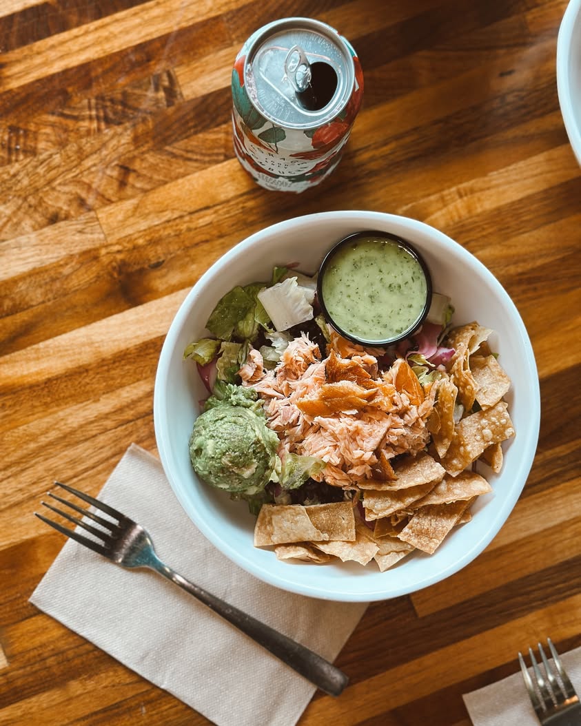An Avocado Crunch Bowl at Forage Kitchen topped with tortilla chips for extra crunch, served alongside a can of kombucha on the table.