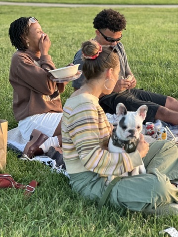 A group of friends sitting in a park with their dog, enjoying grain bowls and wraps from Forage Kitchen outdoors.