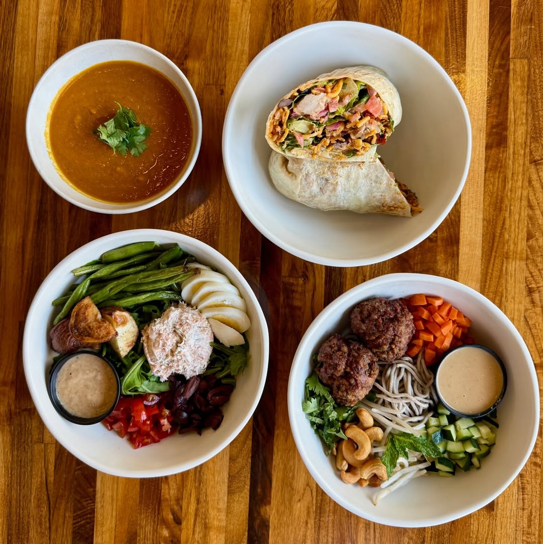 Forage Kitchen lunch spread with a grain bowl, soup, wrap, and salad bowls arranged on a wooden table.