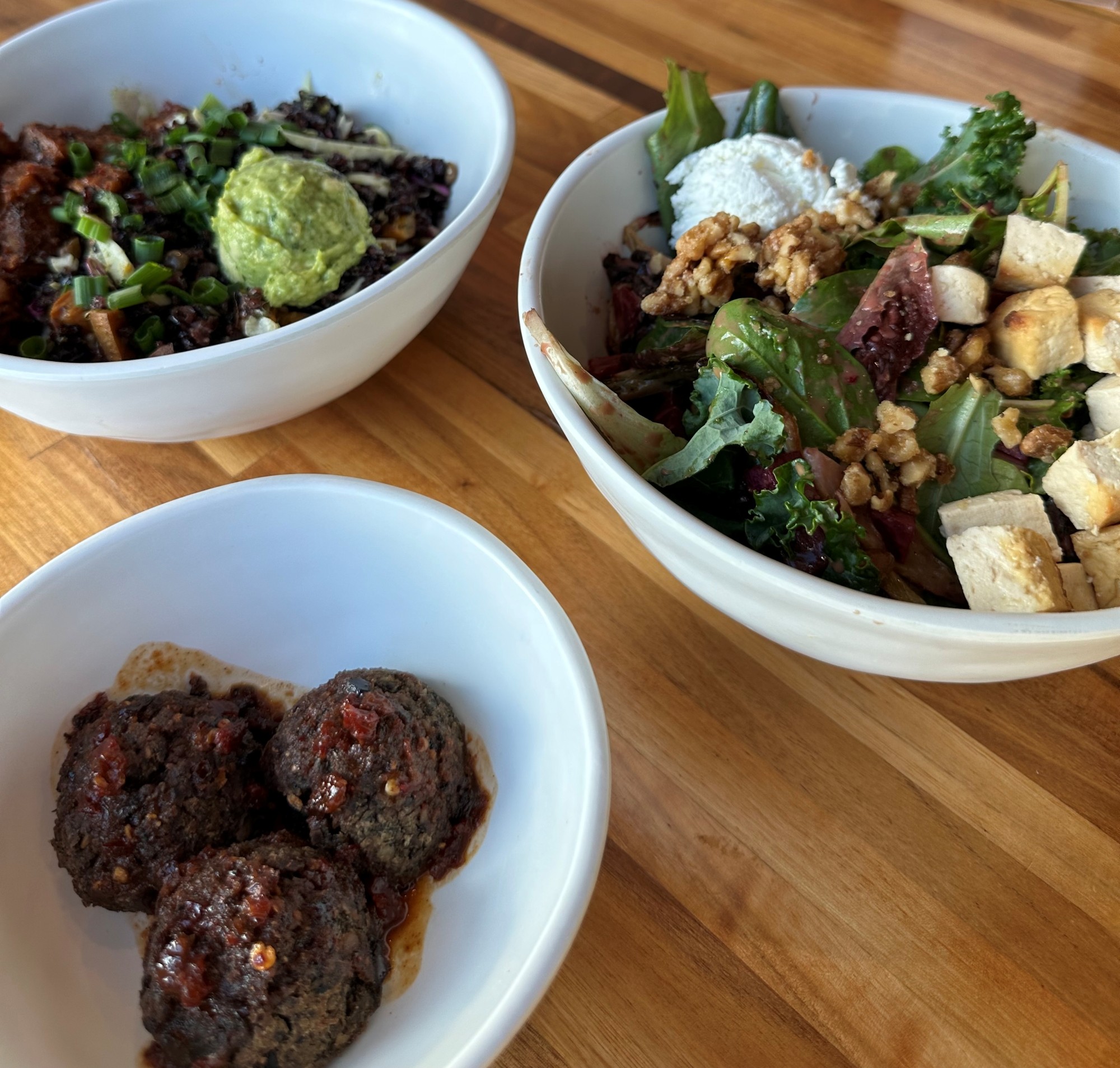 Overhead view of two healthy vegetarian salad and grain bowls and a small bowl of lentil meatballs at Forage Kitchen.