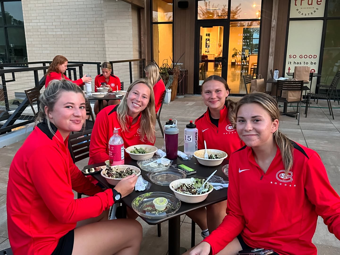 A group of female athletes in red jerseys enjoying grain bowls by Forage Kitchen catering before their game day.
