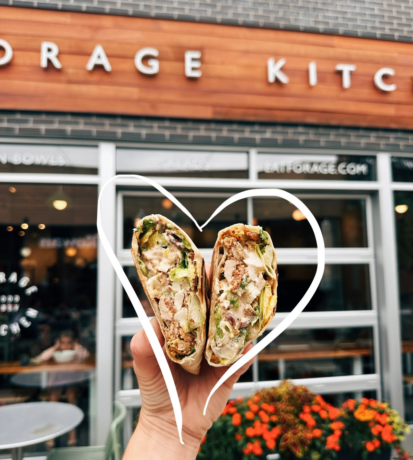 A hand holds two wraps creating a heart shape in front of Forage Kitchen in Madison.