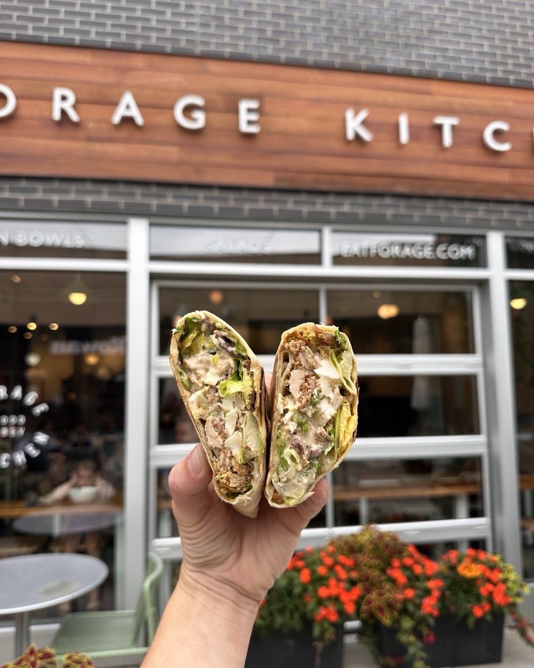 A hand holding a wrap in front of Forage Kitchen.
