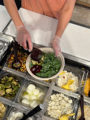 A server at Forage Kitchen assembling a vegan grain bowl with fresh grains, vegetables, and toppings on the prep line.