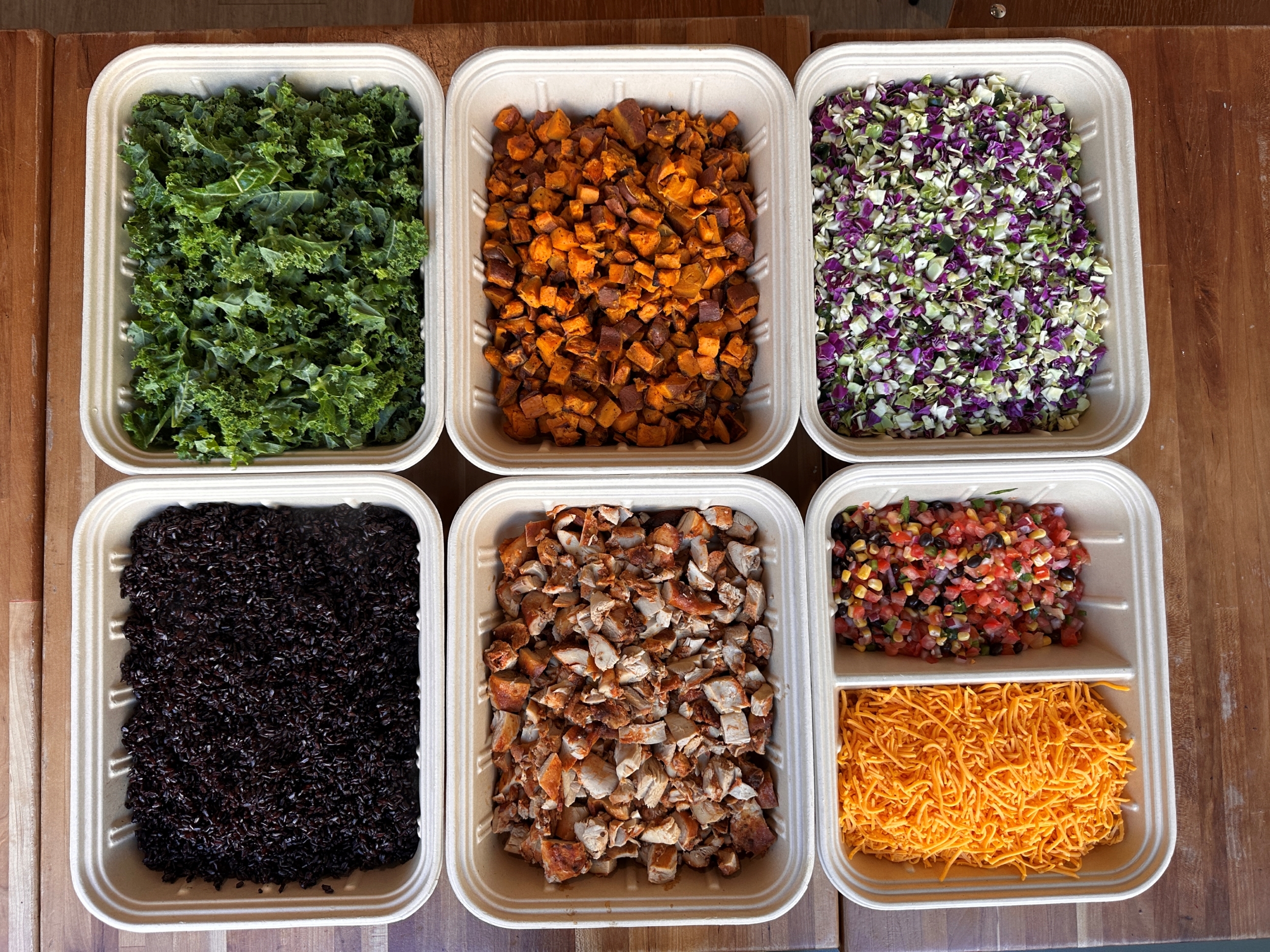 Build-your-own bowl ingredients including kale, sweet potatoes, black rice, and grilled chicken.