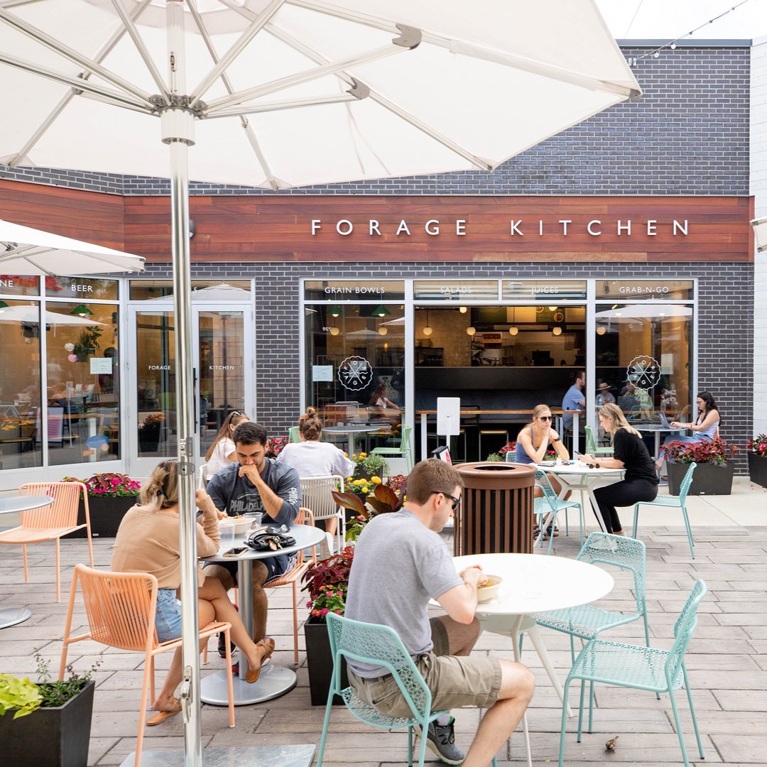 Multiple people dining at the Forage Kitchen restaurant's outdoor patio under large umbrellas.