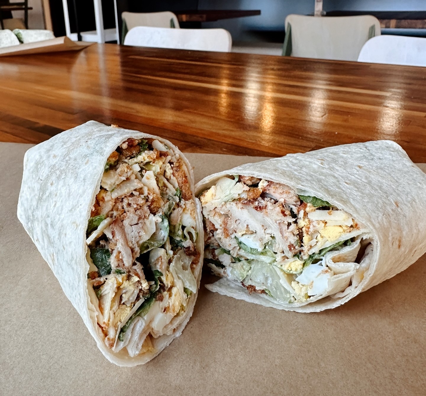  Forage Kitchen Chicken Bacon Caesar wrap, split into two, kept on a table.
