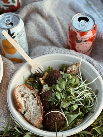 Forage Kitchen bowl with lentil meatballs, fresh greens, sprouts, locally baked sourdough bread, and cans of tepache and kombucha.