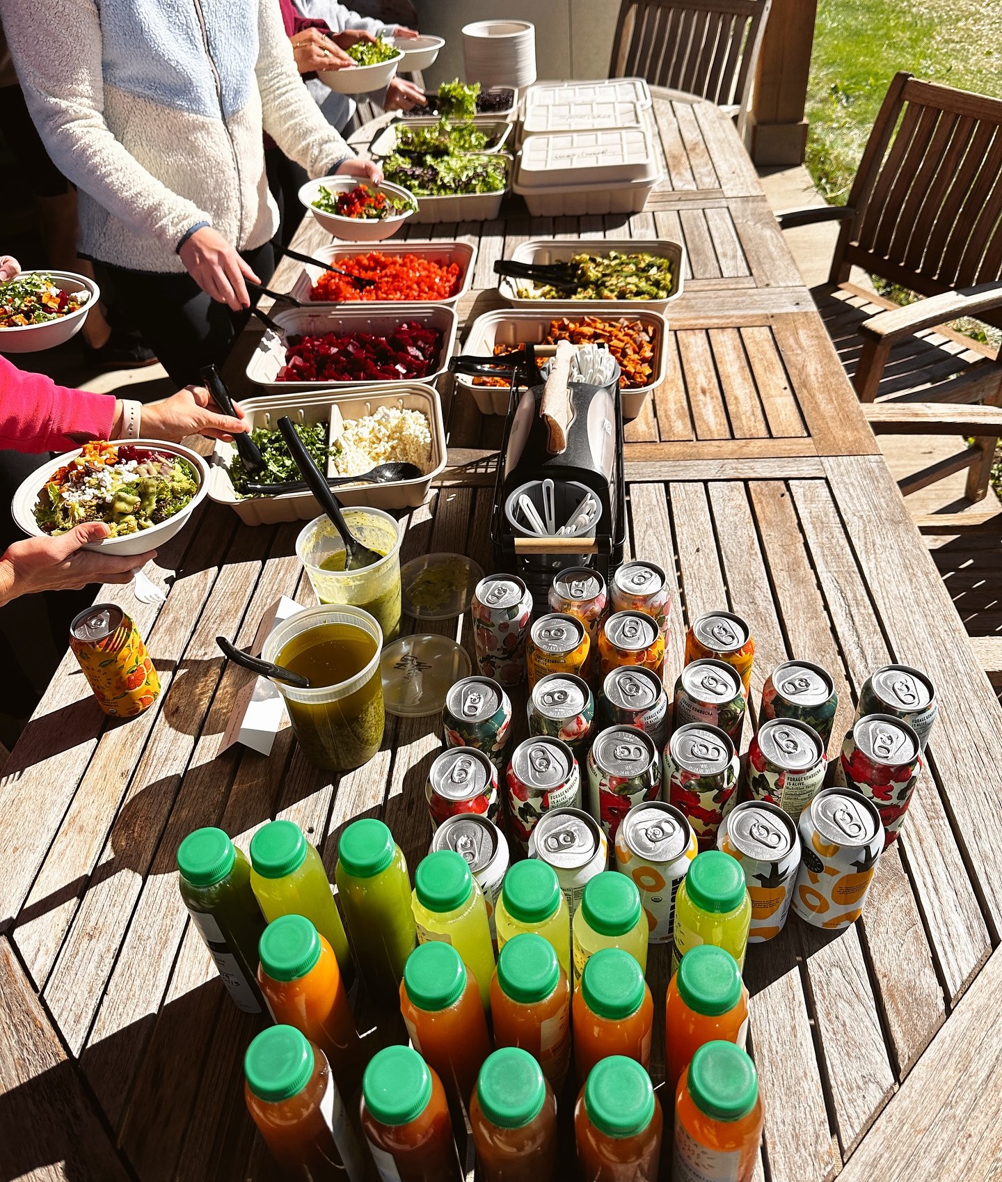 Forage Kitchen catering spread with fresh ingredients, juices, and drinks on an outdoor teak table.