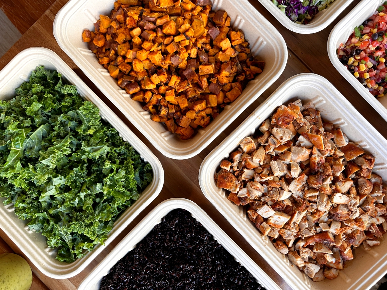 Ingredients for a Build Your Own  catering from Forage Kitchen including kale, sweet potatoes and roasted chicken on a wooden table.