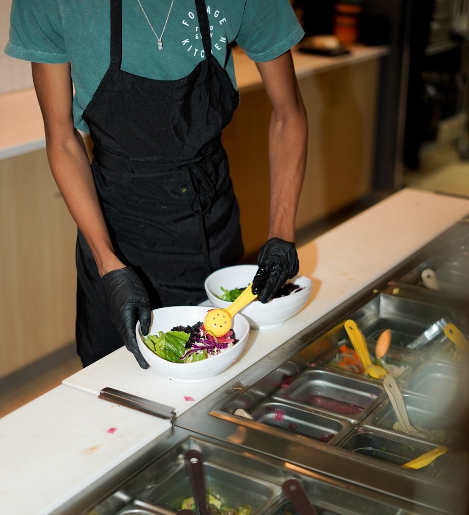 A Forage Kitchen team member wearing a black apron builds a grain bowl for dining in. 