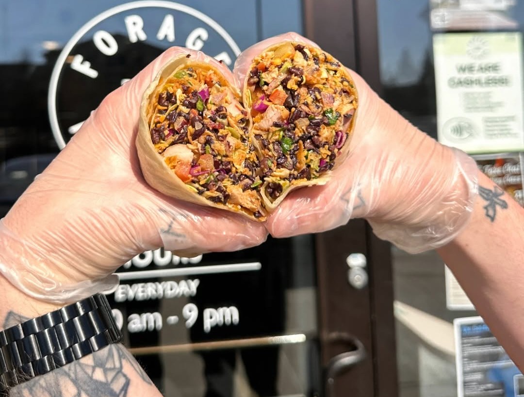 Gloved hands holding Forage Kitchen Santa Fe wrap shaped like a heart in front of the restaurant.