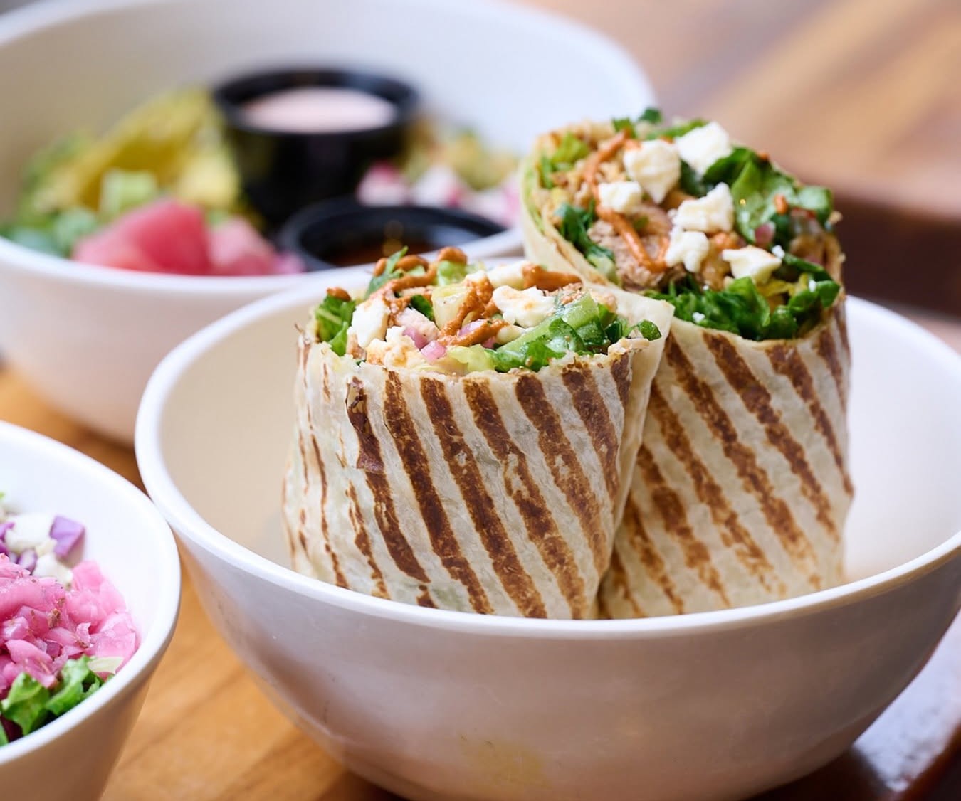 Grilled wrap halves in a bowl with healthy grain bowls in the background at Forage Kitchen.