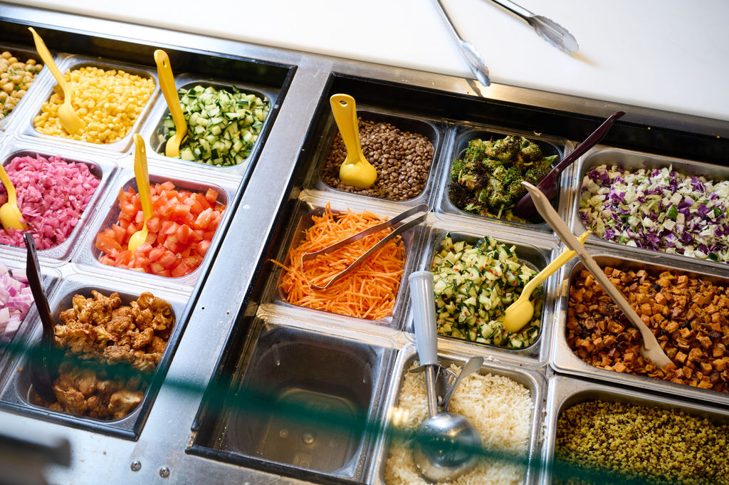 Fresh ingredients with different serving spoons preventing cross-contact at Forage Kitchen Make Your Own Station.
