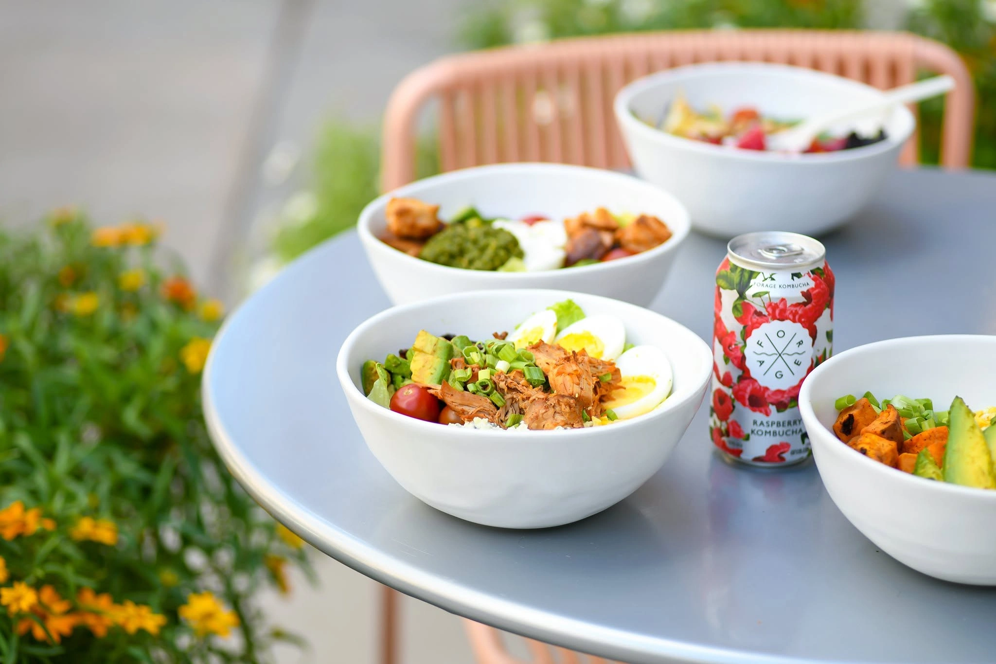 Fresh salad bowls and a kombucha can on an outdoor dining table at Forage Kitchen, Madison.