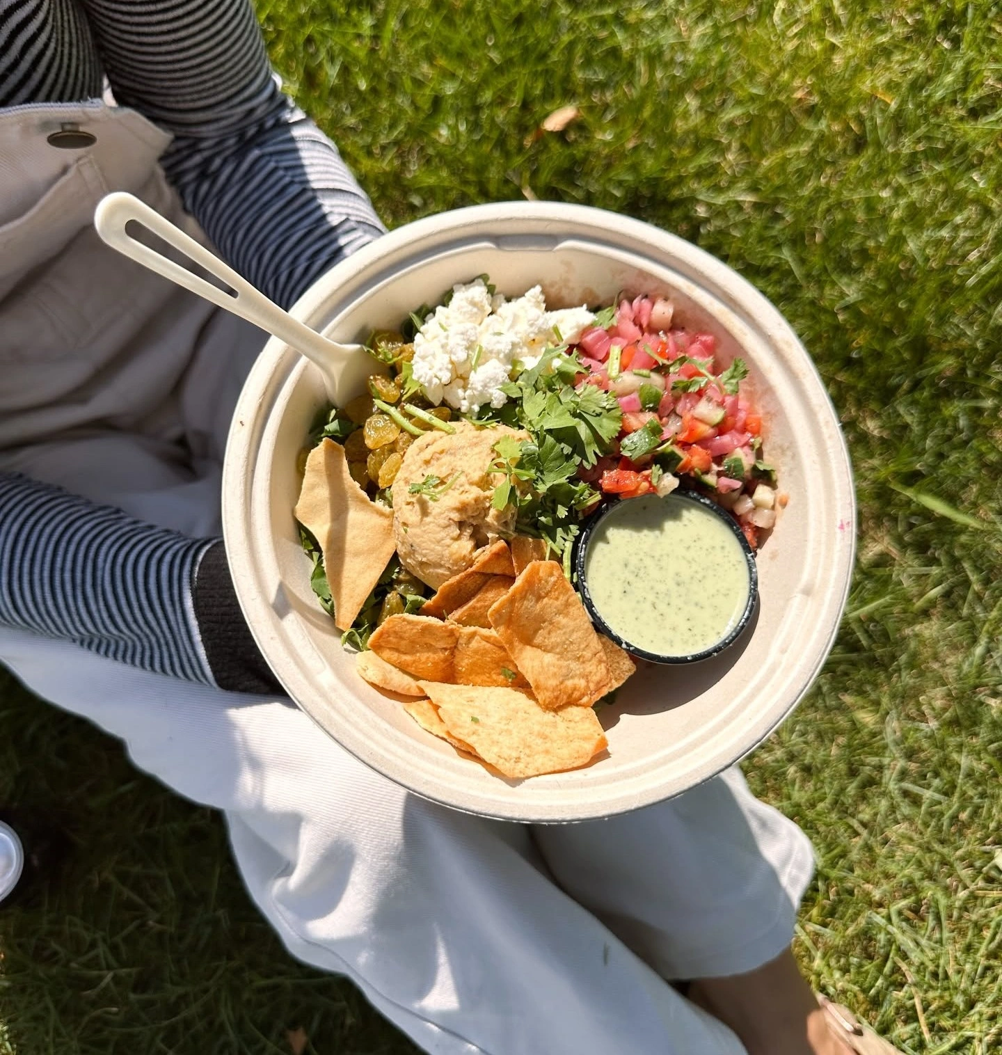 A person holding a fresh bowl from Forage Kitchen for lunch while sitting on the grass.