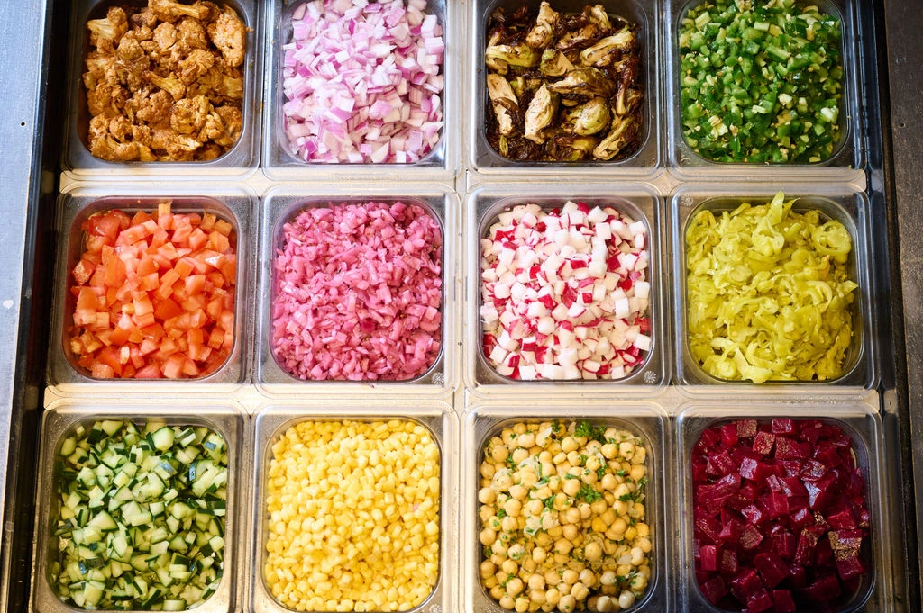  Fresh, colorful whole food ingredients and vegetable toppings organized behind the counter at Forage Kitchen.