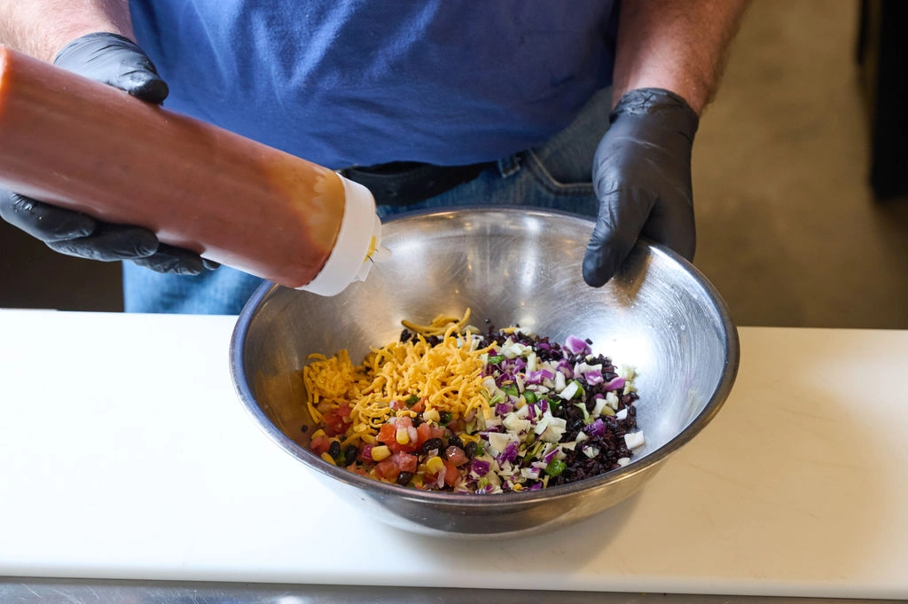 Drizzling signature house-made dressing over a freshly prepared grain bowl at Forage Kitchen.