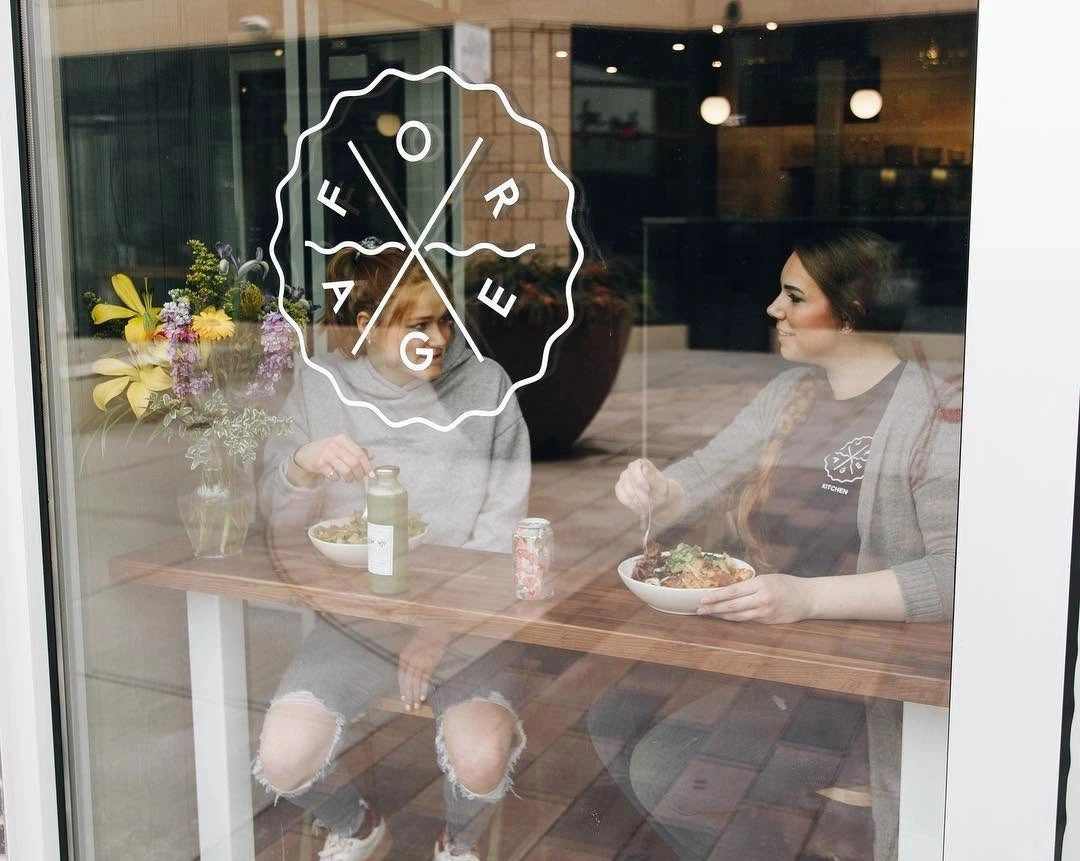 Two women enjoying grain bowls at a window counter inside Forage Kitchen, Hilldale.