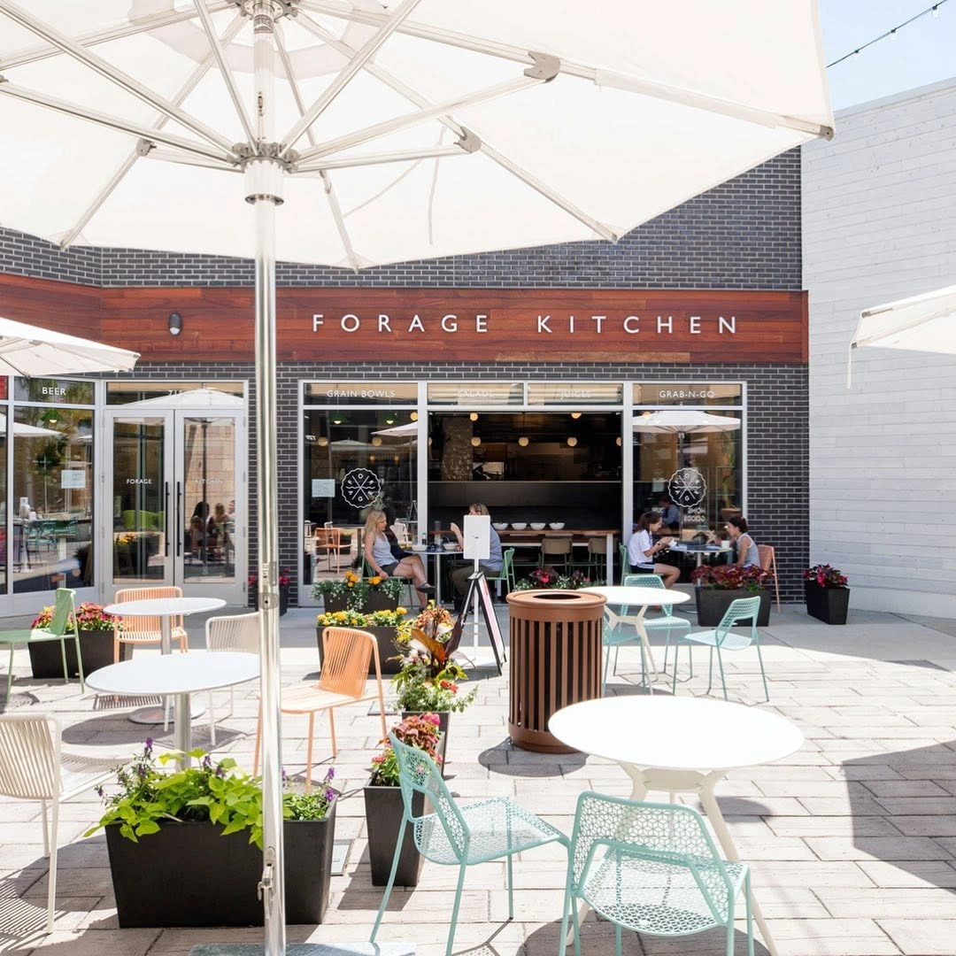 Bright outdoor patio with white umbrellas and tables outside Forage Kitchen at Hilldale.
