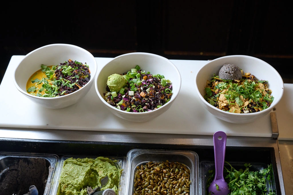 Three grain bowls including Thai, power, and Fiesta bowls lined up on a counter at Forage Kitchen.
